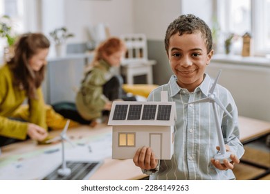 Little boy posing with model of wind turbine and model of house with solar system during a school lesson. - Powered by Shutterstock