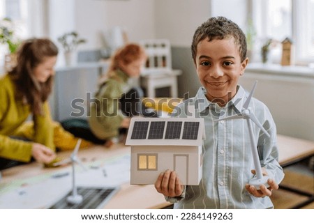 Little boy posing with model of wind turbine and model of house with solar system during a school lesson.