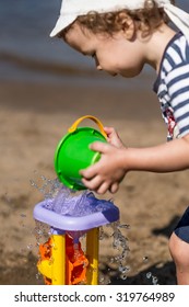 Little Boy Pours Water On The Water Mill On The Beach, Summer