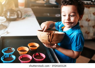 A little boy prepares chocolate muffin dough. The kid licks the chocolate off the spoon. Leisure with children at home. - Shutterstock ID 1924165124