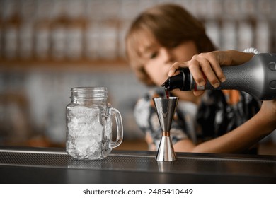 Little boy prepares a fruit cocktail with ice. He pours brown syrup into the jigger from the bottle - Powered by Shutterstock