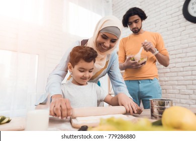 A little boy is preparing a pizza dough with his mother. This is an arab family. Next to them in the kitchen is the father. Family cooking concept.