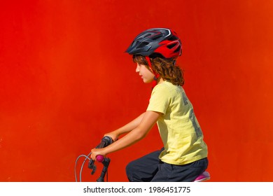 Little Boy In Profile On Red Background Riding Bike With Safety Helmet. Fun And Activity Concept