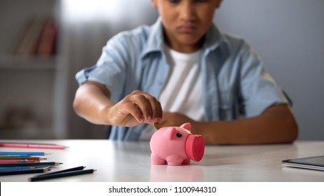 Little boy putting pocket money in piggy bank, raising funds for desired toy