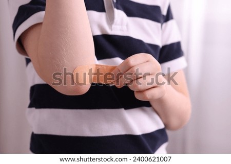 Little boy putting sticking plaster onto elbow indoors, closeup