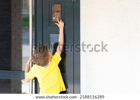 A little boy reaches for the bell to ring the doorbell, a view from the back, copy space. A child standing near the front door of the house. The child returns home.