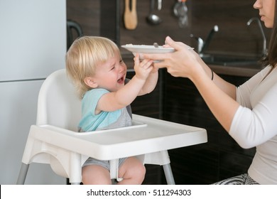 Little boy refuses to eat, he cries and pushes the plate. Mother feeding her child. First solid food for year-old kid. Baby sitting on high chair or rental. Mom and little boy eat porridge