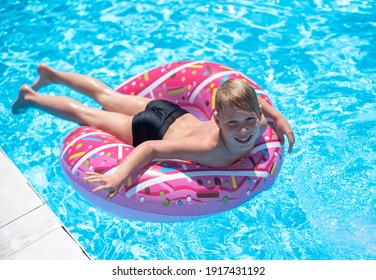 Little boy relaxing on a pool lounger. Pool time, blue water, shark board shorts