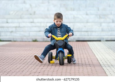 little boy ride toy motorcycle on sidewalk