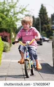 A Little Boy Rides His Bike On The Sidewalk.