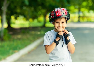 Little Boy Riding On Rollers In The Summer In The Park. Happy Child In Helmet Learning To Skate. Safety In Sport.