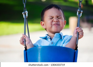 Little Boy Riding A Playground Swing With An Expression Of Fear, Holding On With A Tight Grip Because He Is Scared.