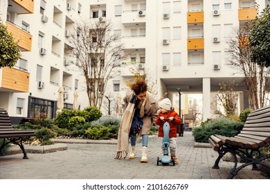 A Little Boy Riding A Scooter And Playing Outside While His Nanny Babysitting Him And Taking Care Of Him Outside.