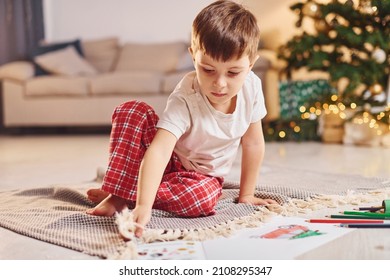 Little boy is in room with christmas tree is on the floor.