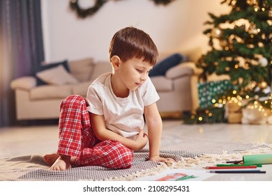 Little boy is in room with christmas tree is on the floor.