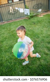 Little Boy Running Around With A Ball On The Grass Near The House