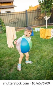 Little Boy Running Around With A Ball On The Grass Near The House