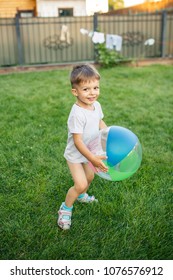 Little Boy Running Around With A Ball On The Grass Near The House