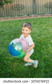 Little Boy Running Around With A Ball On The Grass Near The House