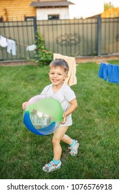 Little Boy Running Around With A Ball On The Grass Near The House