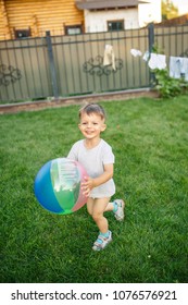 Little Boy Running Around With A Ball On The Grass Near The House