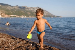 Little Boy Runs Along The Sandy Shore With A Toy Sprinkler