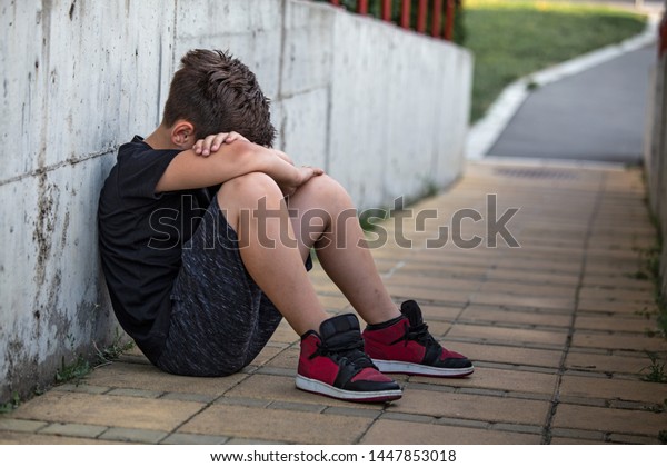 Little boy sad sitting alone at school hides his face. Isolation and bullying concept. Kid sad and unhappy, child was crying, upset, feel sick