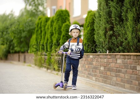 Little boy in safety helmet is riding scooter to school. Quality protect equipment for safety kids on street of city. Back to school and education for children concept.