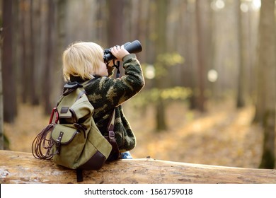 Little boy scout with binoculars during hiking in autumn forest. Child is sitting on large fallen tree and looking through a binoculars. Concepts of adventure, scouting and hiking tourism for kids. - Powered by Shutterstock