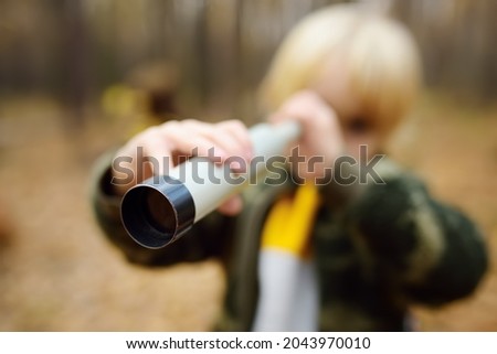 Little boy scout with spyglass during hiking in autumn forest. Child looking through a spyglass. Baby exploring nature. Concepts of adventure, scouting and hiking tourism for kids. Focus on spyglass