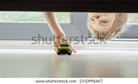 Little boy searching and taking his toy car lost under the bed.