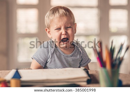 Little boy is seating at table and crying