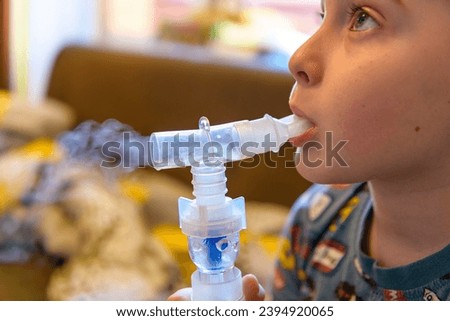 A little boy in selective focus suffering from cough and bronchitis receives breathing treatment using an aerosol inhaler. Treating complications of viral diseases.