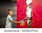 Little boy shaking hands with a humanoid robot while visiting science museum. Concept of modern technologies and children