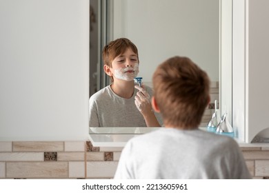 Little Boy With Shaving Foam On Face Imitates His Dad Shaves His Beard. Reflection In Mirror. Face Care.