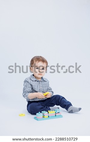 A little boy in a shirt is building a colorful wooden toy on a white background. The concept of children's development, games for children, toys. Copy space