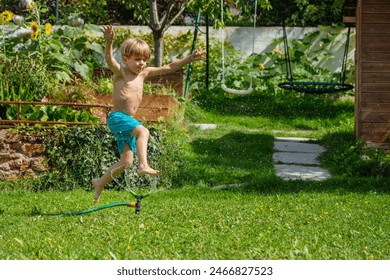 A little boy shirtless having fun while skipping over a sprinkling hose in his backyard garden on summer vacations - Powered by Shutterstock