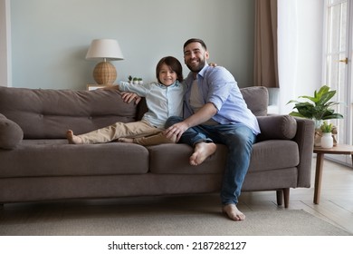 Little Boy Sit On Cozy Sofa With Young Loving Bearded Father, Daddy Spend Weekend With Preschooler 6s Son Smile Look At Camera. Leisure Together, Happy Fatherhood, Understanding, Family Bond Concept