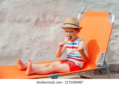 Little Boy Sit In Orange Sunbed And Eats Ice-cream