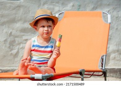 Little Boy Sit In Orange Sunbed And Eats Ice-cream