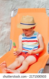 Little Boy Sit In Orange Sunbed And Eats Ice-cream