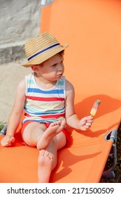 Little Boy Sit In Orange Sunbed And Eats Ice-cream