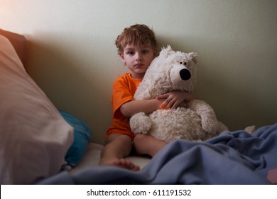 The Little Boy Sits In A Bed With The Toy A Bear. Kid Bad Dream. Bad Mood