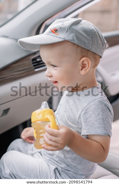 Little boy\
sits in a car and holds a bottle of juice in his hand Portrait of a\
child with blue eyes in sunny\
weather