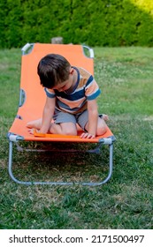 Little Boy Sits On Orange Sunbed In Outdoor 