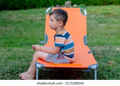 Little Boy Sits On Orange Sunbed In Outdoor 