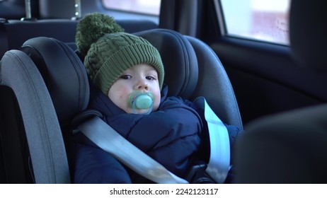 A little boy is sitting in a child seat in a car. A baby travels in a car in winter. Boy in jacket and hat. - Shutterstock ID 2242123117