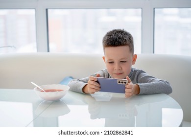 Little Boy Sitting At The Dinner Table And Playing The Phone