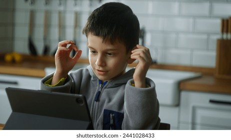 Little boy sitting in the kitchen playing mobile game on digital tablet device reacting to lose game. Child surfing internet, play game at home. Children tech addiction concept - Powered by Shutterstock