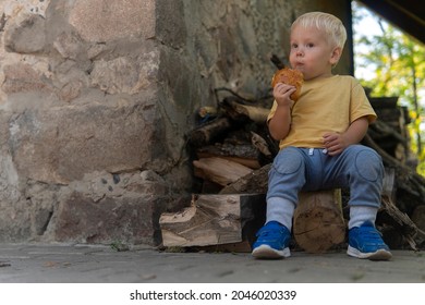 Little Boy Sitting Near The House And Eating Pie.